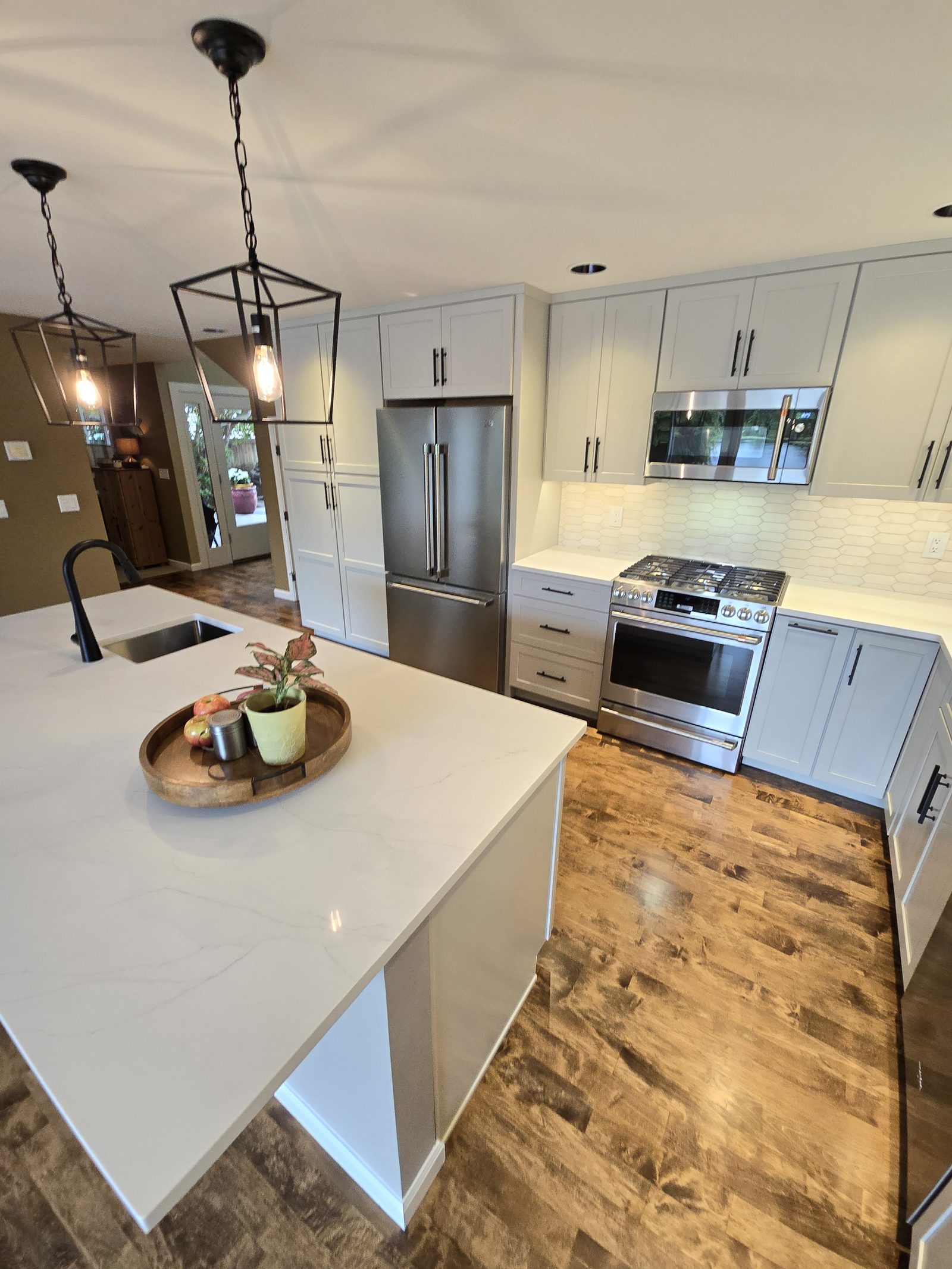 Kitchen after remodel - white shaker cabinets, quartz countertops, dark wood floors